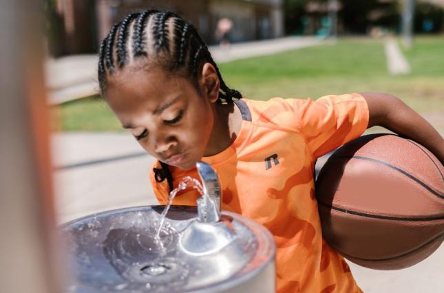 image of a kid drinking from a fountain (canva image)