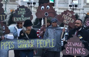 People rallying in front of Baltimore City Hall holding signs like "Pipes should work for People."