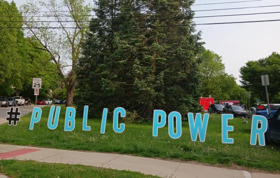 Large cut out letters spelling #PUBLICPOWER on grass outside Ann Arbor for Public Power rally, Burns Park 2023