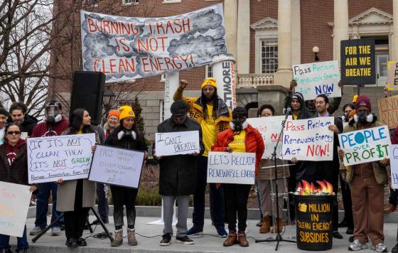 Picture of people protesting in Annapolis holding signs like "Burning trash is not clean energy," "For the air we breathe," "Let's Reclaim Renewable Energy."